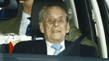 an older man in a suit and tie is sitting in a car