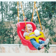 a baby is sitting on a red swing holding a toy