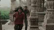 a man and a woman are running through a building with columns