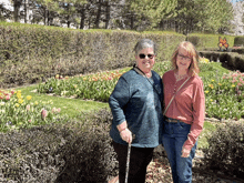 two women are standing in front of a flower garden