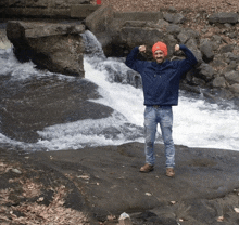 a man stands in front of a waterfall with his arms up