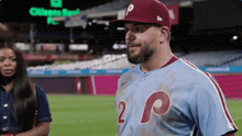 a man in a baseball uniform is standing on a baseball field with a woman in the background .