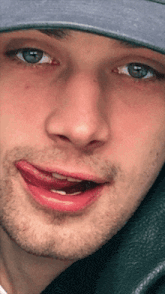 a close up of a man wearing a hat with his tongue out
