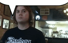 a man wearing a bodega shirt stands in a restaurant