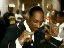 snoop dogg is wearing a suit and tie and smoking a cigarette in a crowd of people .