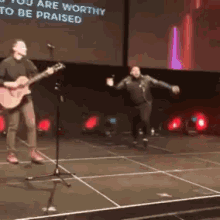 a man playing a guitar on a stage with the words " you are worthy to be praised " on the screen