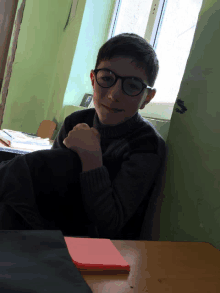 a boy wearing glasses is sitting at a desk