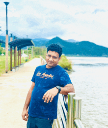 a man wearing a blue los angeles t-shirt leans against a railing