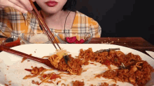 a woman is eating noodles with chopsticks and a spoon .