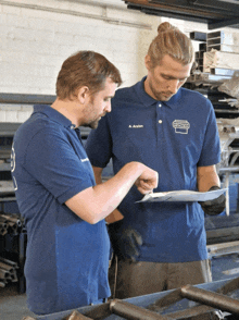 two men are looking at a piece of paper and one has a shirt that says a. arslan on it