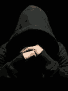 a person in a hoodie is covering their face with their hands in the dark .