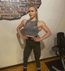 a woman stands with her hands on her hips in front of a brick wall that has the word muscles written on it