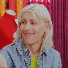 a man with blonde hair and pink eyebrows wearing a denim jacket