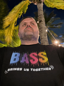 a man wearing a shirt that says " brings us together " stands in front of a palm tree