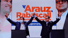 two men are holding hands in front of a screen that says arauz rabascall