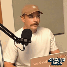 a man wearing a hat and a white shirt is sitting in front of a microphone and a laptop that says washed