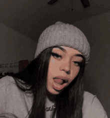 a girl wearing a gray beanie and a gray sweater is sticking her tongue out .