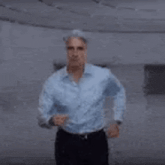 a man in a blue shirt and black pants is standing in front of a gray wall .