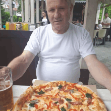 an older man sits at a table with a pizza and a glass of beer