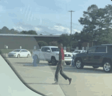 a man in a red shirt is walking across a parking lot