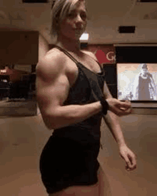 a woman with very muscular arms is standing in front of a television .