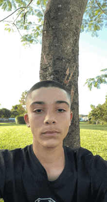 a young man in a black shirt is taking a selfie in front of a tree