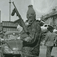 a man in a mask is holding a gun in front of a car .