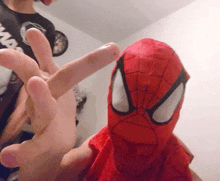 a person in a spiderman costume is giving a peace sign while holding a stuffed animal .