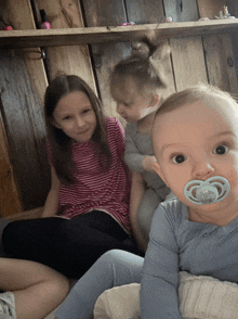 a baby with a pacifier in his mouth is sitting next to two little girls