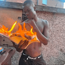 a shirtless man wearing nike shorts holds a burning piece of paper