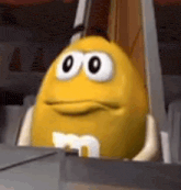 a yellow m & ms cartoon character with big eyes is sitting in a box .