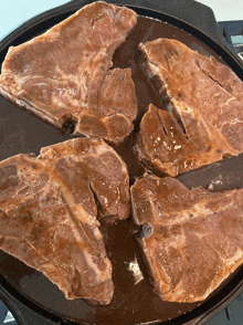 four pieces of meat are cooking in a pan on a stove top