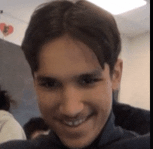 a close up of a man 's face smiling with a heart hanging from the ceiling behind him .