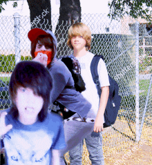 a boy in a blue shirt is standing in front of a fence