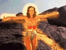 a woman in a wonder woman outfit is standing on a rocky hillside with her arms outstretched