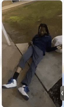 a man with dreadlocks is laying on the sidewalk with his legs crossed .