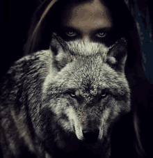 a woman is standing next to a wolf with a wolf covering her face .