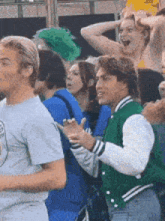 a man in a green varsity jacket stands in a crowd of people .