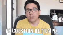 a man wearing glasses and a yellow shirt is sitting in a chair with the words es cuestión de tiempo above him