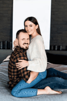 a woman is sitting on a man 's lap on a bed and smiling