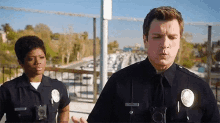 a man and a woman in police uniforms are standing next to each other and talking .