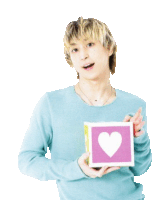 a man in a blue sweater is holding a pink square with a heart on it