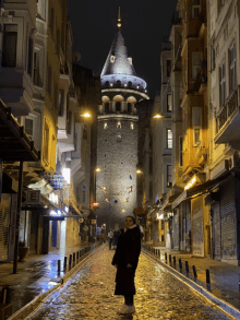 a woman stands on a cobblestone street in front of a tower