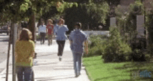 a group of people are walking down a sidewalk with trees in the background .