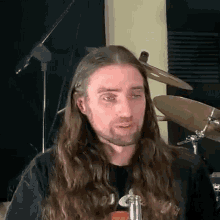 a man with long hair and a beard is sitting in front of a drum set in a recording studio .