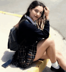 a young woman in a school uniform is sitting on a curb with her legs crossed .