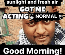 a man with a scarf around his neck is standing in front of a brick building with a good morning message on it .