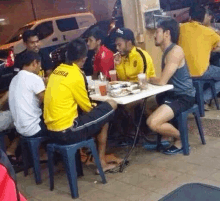 a group of men are sitting around a table eating food and drinking .