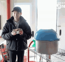 a man in a black jacket is holding a bowl of food while standing next to a blue bowl .