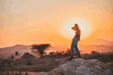 a person standing on top of a rock at sunset with the sun behind them